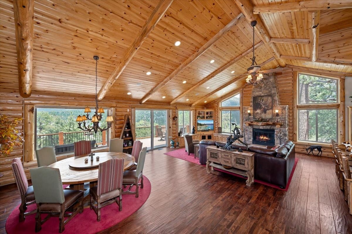 Vaulted log-beam great room with stone fireplace and forest views