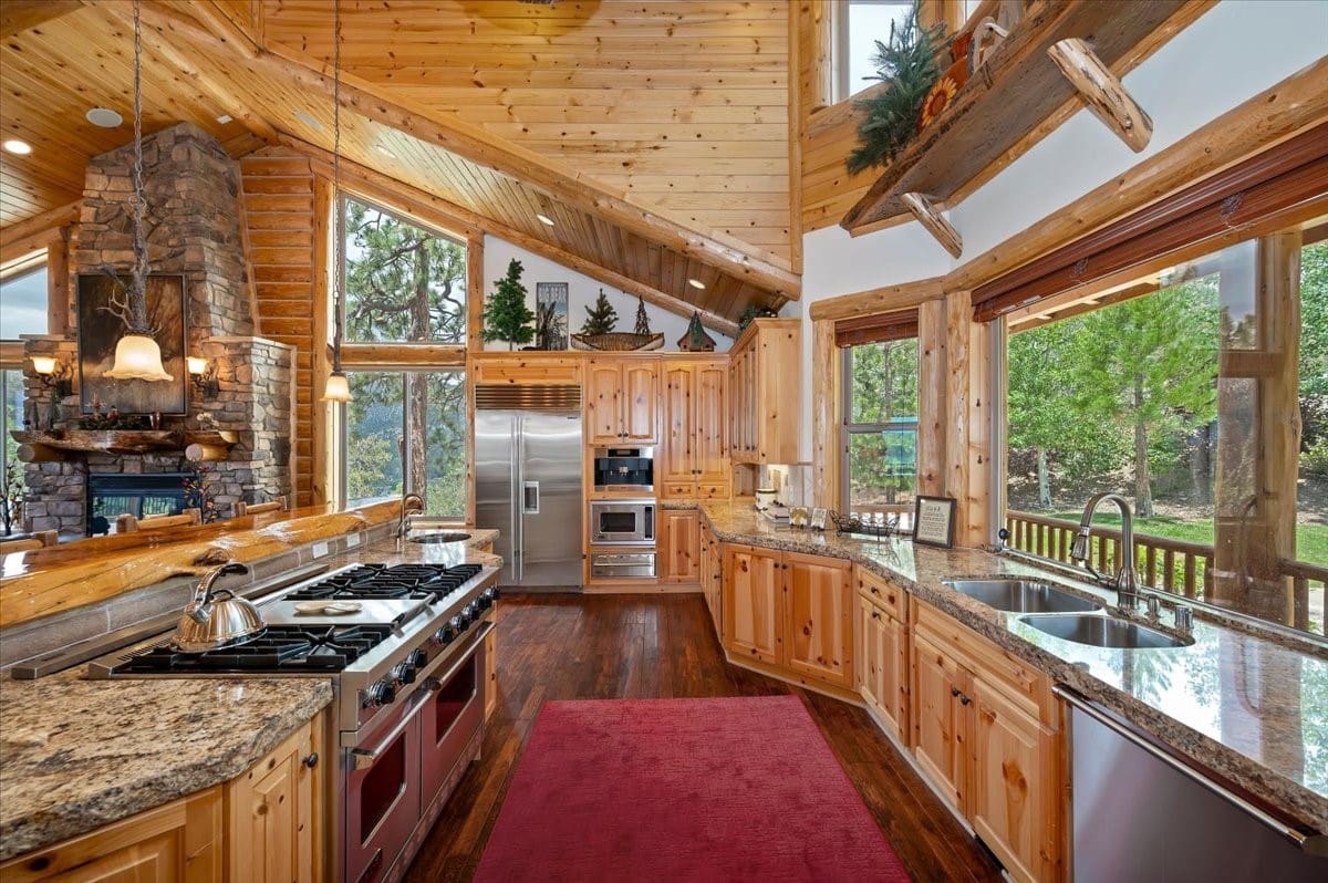 Log cabin chef's kitchen with stone fireplace and forest views