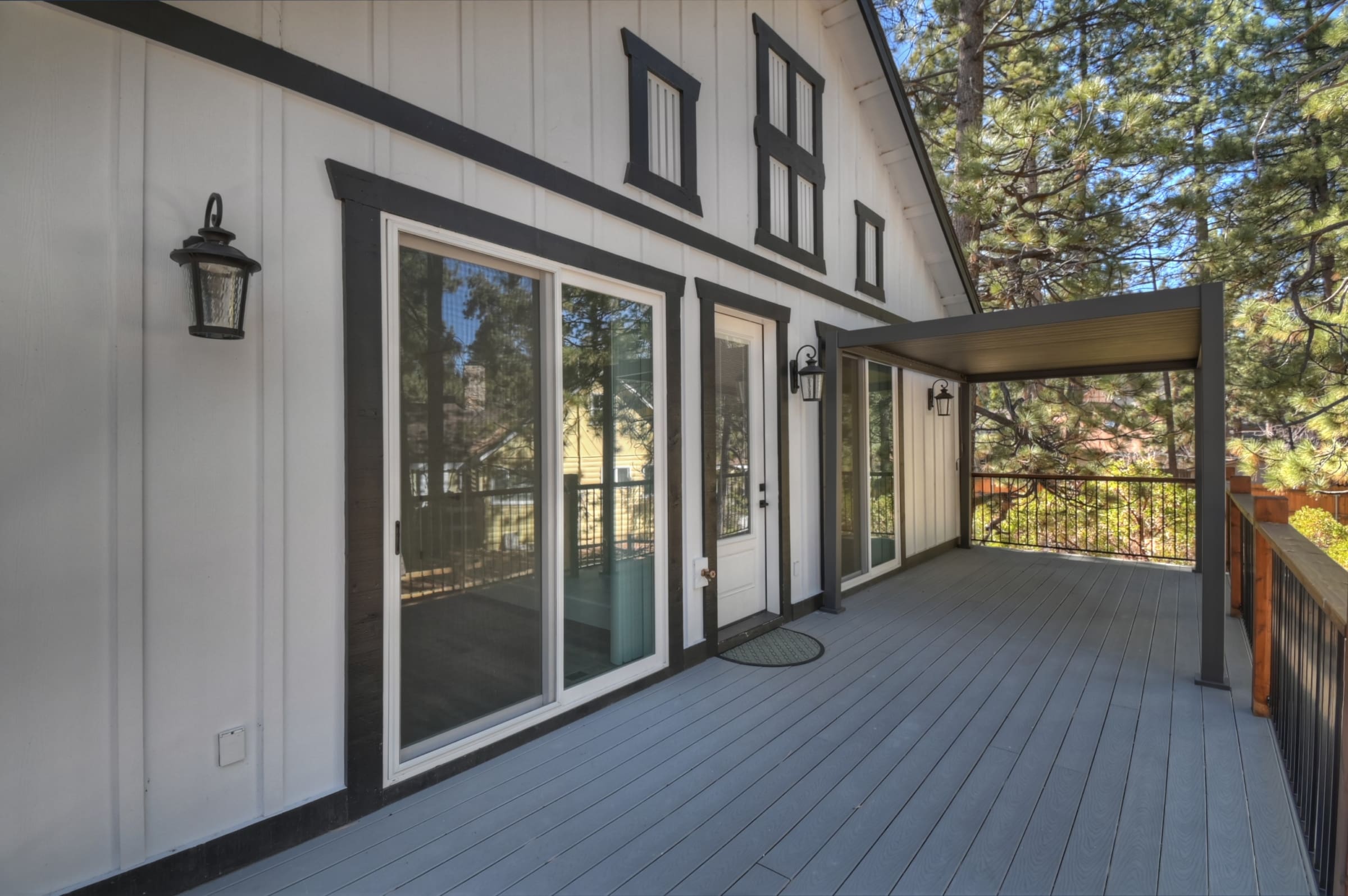 Covered deck with sliding glass access, framed by tall pines